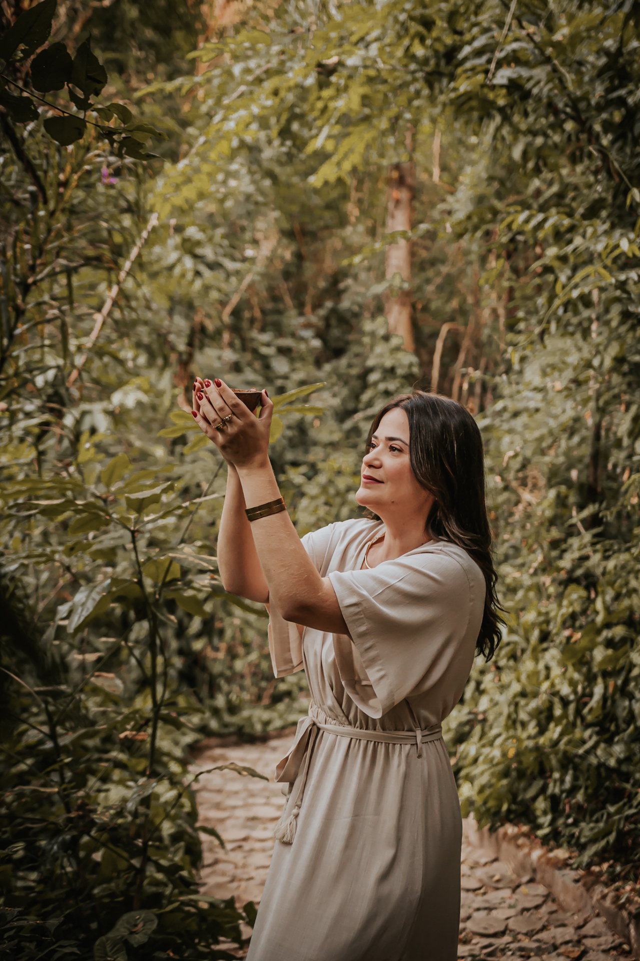 Viviane Moraes segurando uma tigela de coco com cacau quente, em meio à natureza, luz dourada